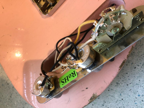 Close-up of vintage guitar electronics with potentiometers and wiring on pink guitar body, showing detailed internal components and RoHS compliance sticker.