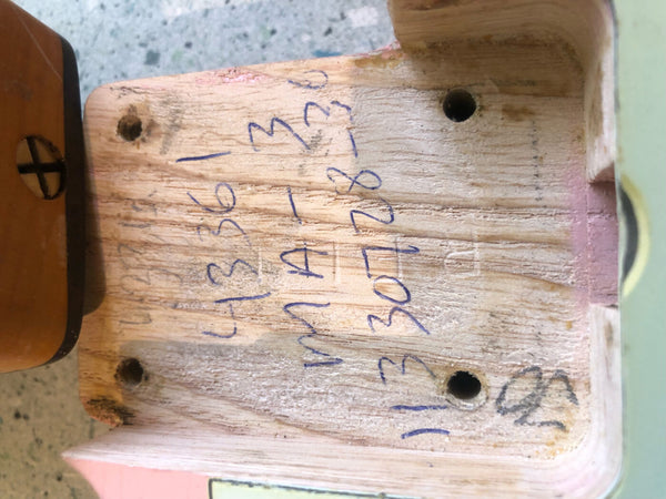 Close-up of the neck pocket of a guitar body showing handwritten notes and markings on unfinished wood around four screw holes near the neck joint area.