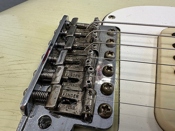 Close-up of vintage Fender guitar bridge and saddles showing strings and screws on white electric guitar body