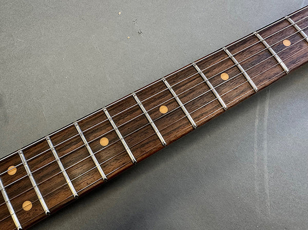 Close-up of dark wooden guitar fretboard with metal frets and dot inlays on gray surface