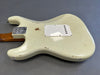 Back view of vintage off-white electric guitar body with worn paint and metal neck plate on gray surface
