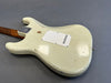 Vintage white electric guitar body with worn paint and wooden neck on gray surface, rear view