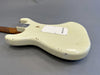 Vintage cream electric guitar body with worn and chipped finish, showing relic wear, lying flat on gray surface, rear view