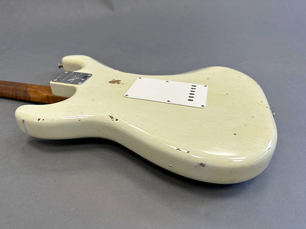 Vintage cream electric guitar body with worn and chipped finish, showing relic wear, lying flat on gray surface, rear view