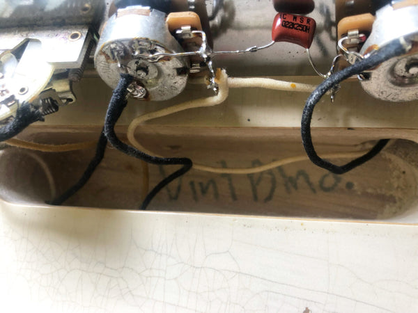 Close-up of vintage guitar potentiometers and wiring inside guitar control cavity with visible handwritten "Vint Dino" marking on wood cavity wall