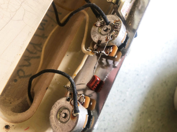 Close-up of vintage electric guitar control cavity showing potentiometers, wiring, and capacitor components inside the metal control plate.