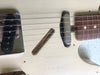 Close-up of white vintage relic electric guitar body showing worn finish, metal bridge, single coil pickups, and rosewood fretboard with dot inlays