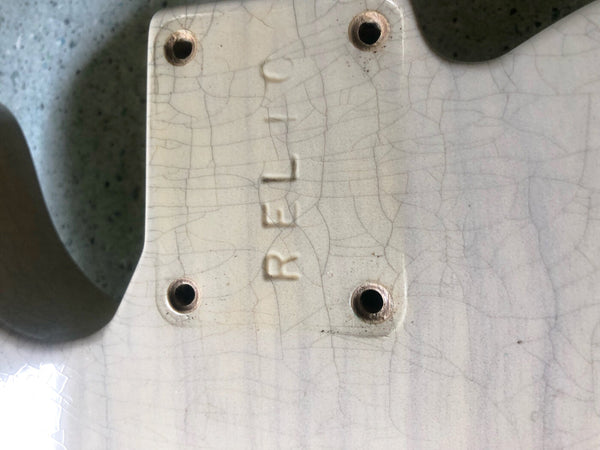 Close-up of vintage cream guitar body with "REFL" embossed near neck plate screw holes and visible aging cracks in the finish