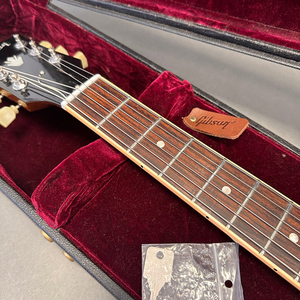 Close-up of Gibson guitar rosewood fretboard and headstock inside velvet-lined hardshell case with Gibson leather tag and accessory bag at Coffee House Guitars