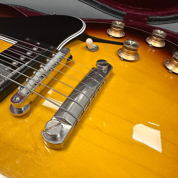 Close-up of sunburst electric guitar body showing chrome bridge, strings, white toggle switch, and amber control knobs with volume markings, inside a velvet-lined case.