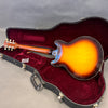 Sunburst semi-hollow electric guitar resting in open black hard case with red velvet interior, showing back and neck of guitar.