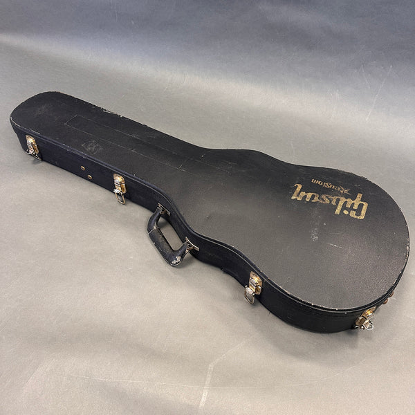Vintage black Gibson guitar hard case with gold logo and metal latches on gray background