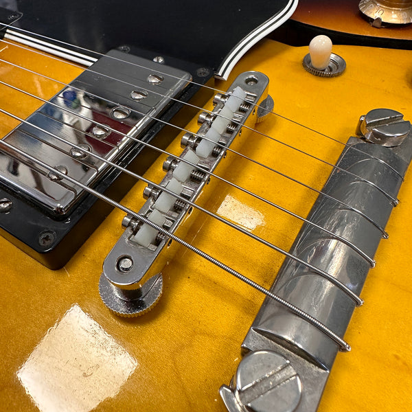Close-up of electric guitar bridge, saddle, and pickup on a sunburst finish guitar body with metal hardware and strings.
