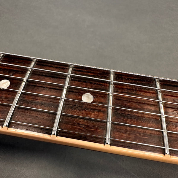 Close-up of rosewood guitar fretboard with metal frets and mother of pearl dot inlays on electric guitar neck