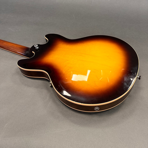 Back view of sunburst semi-hollow body electric guitar with wooden neck on gray surface