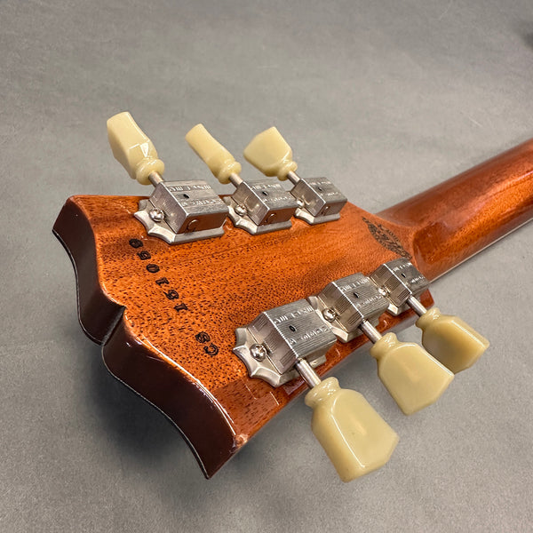 Close-up view of mahogany guitar headstock with vintage tuning pegs and serial number stamped on back