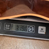 Close-up of digital scale showing 3.196 kilograms with guitar body partially visible on top, highlighting guitar weight for Coffee House Guitars product listing.