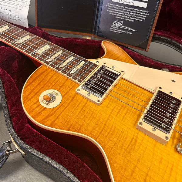 Close-up of sunburst electric guitar with dual humbucker pickups, cream pickguard, and rhythm/treble toggle switch in plush red-lined black hardshell case with certificate of authenticity.