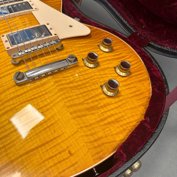 Close-up of honey burst electric guitar body with chrome bridge and four amber control knobs inside red velvet-lined guitar case