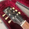 Close-up of Gibson Les Paul guitar headstock with tuning pegs, inside red velvet-lined guitar case