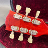 Close-up of guitar headstock back with vintage-style tuning pegs and serial number CS0 60017 on red wood finish in red velvet case interior