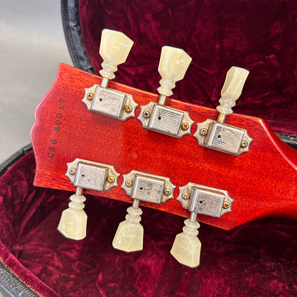 Close-up of guitar headstock back with vintage-style tuning pegs and serial number CS0 60017 on red wood finish in red velvet case interior