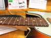 Close-up of Fender electric guitar rosewood fretboard and strings with sunburst finish body and white pickguard, displayed with Fender certification tags in the background on orange plush case lining.