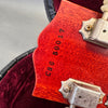 Close-up of guitar headstock with serial number CS0 50017 stamped on reddish wood near vintage metal tuning pegs in guitar case lined with red velvet