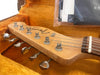 Close-up of Fender Custom Shop Stratocaster guitar headstock with tuning pegs and strings inside an orange plush-lined guitar case