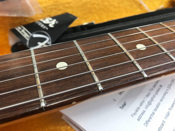 Close-up of rosewood guitar fretboard with metal frets and white dot inlays, guitar strings in focus on wooden background
