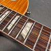 Close-up of amber sunburst electric guitar rosewood fretboard with mother of pearl block inlays and steel strings on gray background