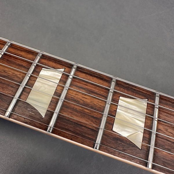 Close-up of guitar fretboard with pearl trapezoid inlays and steel strings on rosewood fingerboard