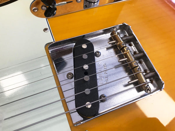 Close-up of Fender bridge and single coil pickup on a yellow electric guitar with six strings and chrome hardware