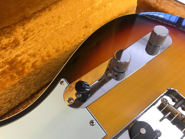 Close-up of sunburst electric guitar control panel with chrome knobs and pickup selector switch on orange plush guitar case background