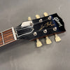 Close-up of Gibson Les Paul Model guitar headstock with vintage tuners and black finish on gray background