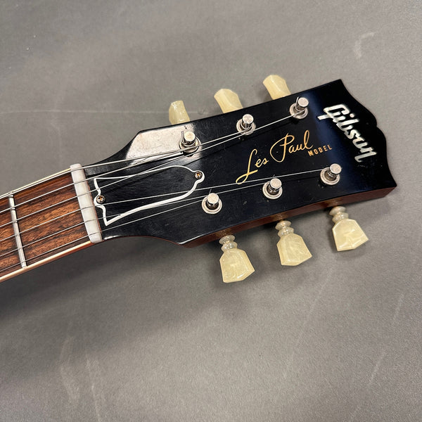 Close-up of Gibson Les Paul Model guitar headstock with vintage tuners and black finish on gray background