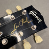 Close-up of Gibson Les Paul Model guitar headstock with vintage tuning pegs and strings against gray background