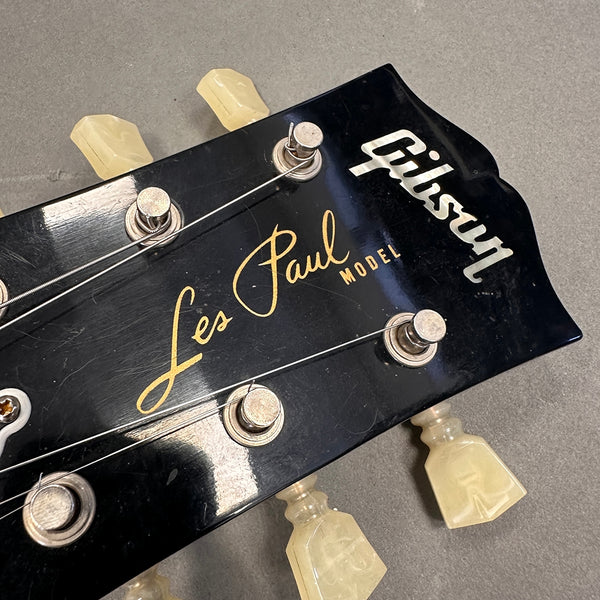 Close-up of Gibson Les Paul Model guitar headstock with vintage tuning pegs and strings against gray background