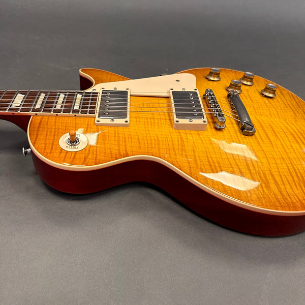 Close-up of sunburst electric guitar with cream pickguard, dual humbucker pickups, and chrome bridge and tailpiece on gray background