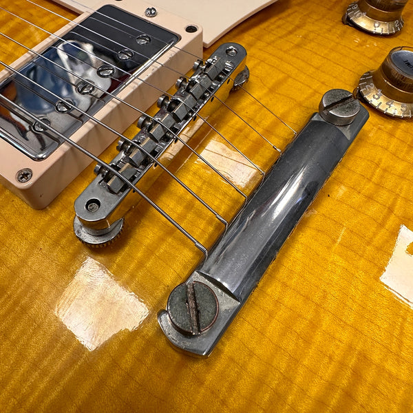 Close-up of electric guitar bridge, tailpiece, and pickup on amber flame maple top with volume and tone control knobs