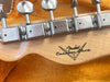 Close-up of Fender Custom Shop guitar headstock back with vintage-style tuning pegs and logo on natural wood grain background