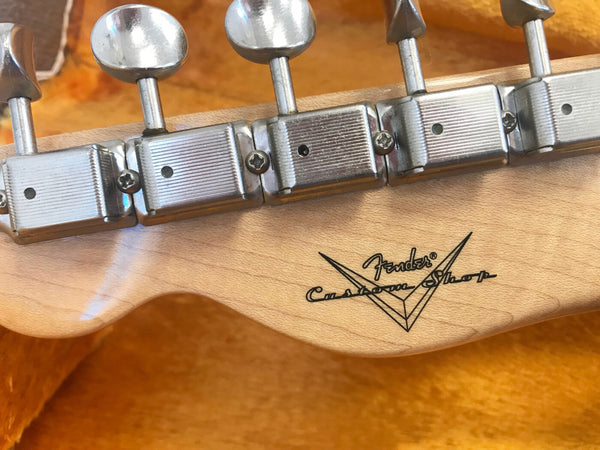 Close-up of Fender Custom Shop guitar headstock back with vintage-style tuning pegs and logo on natural wood grain background