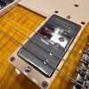 Close-up of electric guitar chrome humbucker pickup on sunburst flamed maple top with visible strings and cream pickup mounting ring