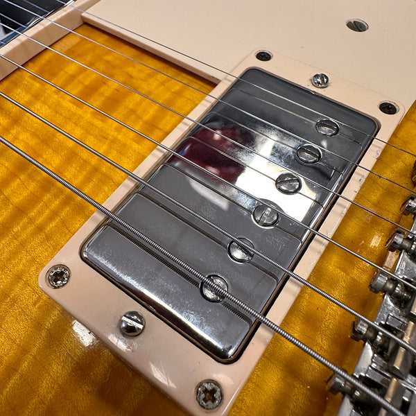 Close-up of electric guitar chrome humbucker pickup on sunburst flamed maple top with visible strings and cream pickup mounting ring