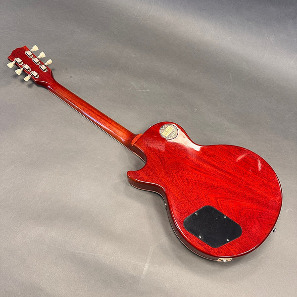 Back view of red Gibson electric guitar showing neck, headstock with tuning pegs, and electronics cavity cover on gray surface