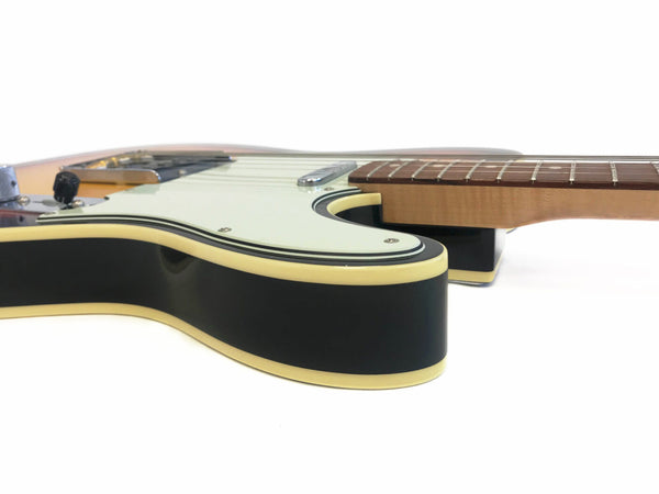 Close-up side view of black electric guitar body with cream binding and white pickguard, maple neck and rosewood fretboard on white background