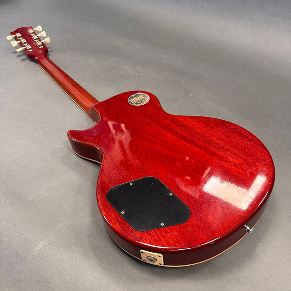 Back view of cherry red Gibson Les Paul electric guitar with black control cavity cover and vintage tuners on gray background