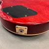Close-up of red electric guitar body showing black backplate and beige output jack plate on gray surface