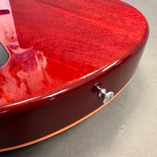 Close-up of glossy red electric guitar body showing wood grain, strap button, and cream binding edge on gray background