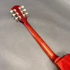 Back view of red wooden guitar neck with six tuning pegs on gray background